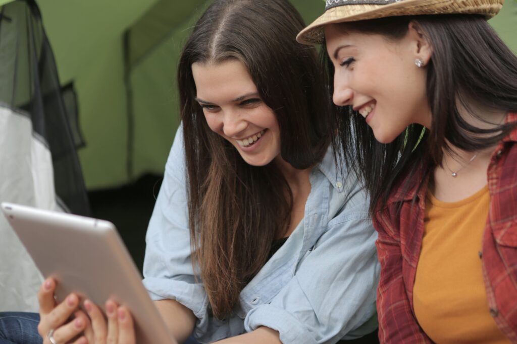 a imagem mostra duas pessoas sorrindo e olhando para um tablet, como duas irmãs vendo mensagem de aniversário emocionante