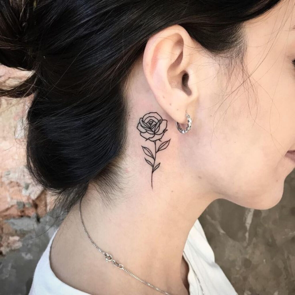 Tatuagem delicada logo atrás da orelha. A mulher fez a tatuagem no pescoço e escolhe uma rosa para marcar a região. O caule está próximo à clávicula e a rosa, próxima a orelha. 