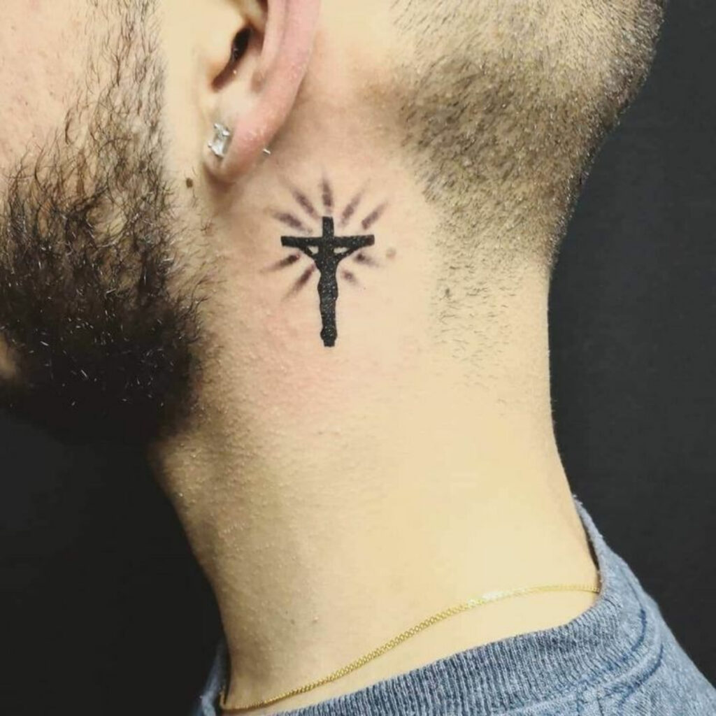 Cruz religiosa tatuada em um homem de pele branca logo abaixo da orelha, na lateral do pescoço. 