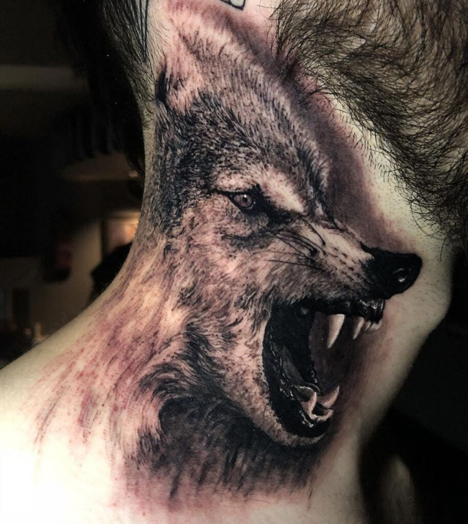 Pescoço de um homem de pele branca completamente tatuado com um lobo que está em posição de ataque. 
