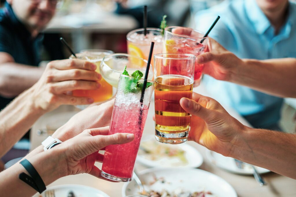 Líquido alcoólico: quatro pessoas brindando com drinks alcoolicoscom as cores vermelhas e amarelas de fundo uma mesa com pratos