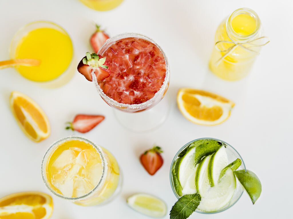 drinks fáceis: mesa branca com frutas citricas sobre ela, Laranja e cascas de laranja, copos de suco de laranja e morango