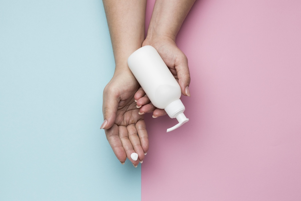 Sabonete líquido intimo: mãos femininas , a mão esquerda está segurando o sabonete líquido, o fundo da imagem é um fundo dividido meio a meio nas cores azul bebe e rosa pastel 