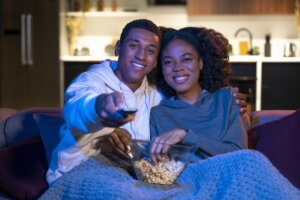 Filmes de Ano Novo: casal assistindo à televisão juntos. Eles estão abraçados com pote de pipoca nas mãos
