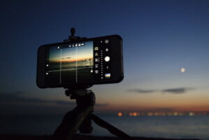 Como tirar foto da lua: câmera no suporte tirando do céu noturno. O céu aparece em um tom de azul mais claro na mais acima e em um tom de laranja mais abaixo.