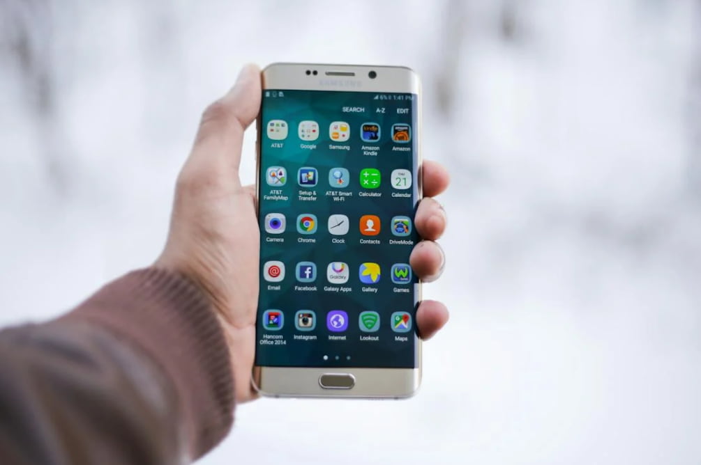 Mão segura celular Samsung ligado com vários aplicativos após ver como desbloquear celular sem senha