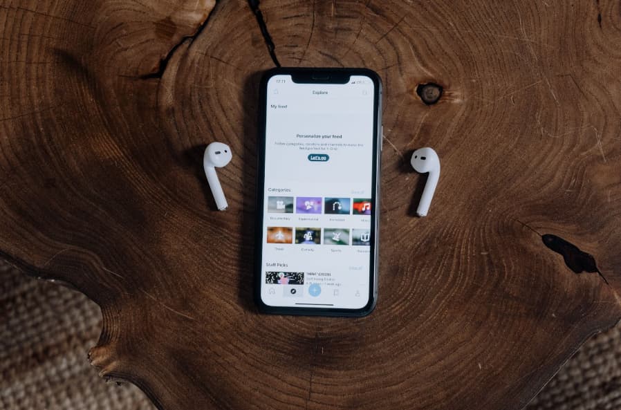 celular em cima de mesa de madeira com fones de ouvido procurando aplicativos de música 